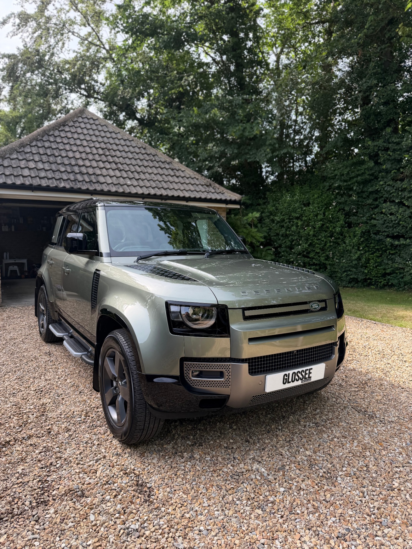 Satin green Land Rover Defender front three-quarter on gravel driveway